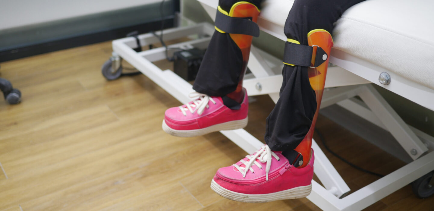 Child's legs with orthopedic braces and bright pink shoes on clinic bed